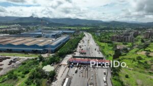 PD0756 - Aerial Shot of a Highway Toll Plaza Near an Industrial Complex with a Mountain Backdrop