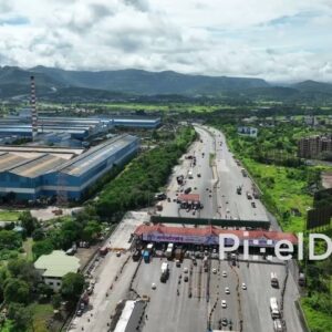 PD0756 - Aerial Shot of a Highway Toll Plaza Near an Industrial Complex with a Mountain Backdrop