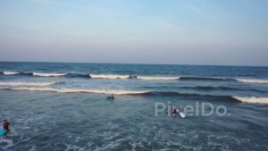 PD0978 - Aerial Pan of Surfers Learning to Ride Waves at Sunset